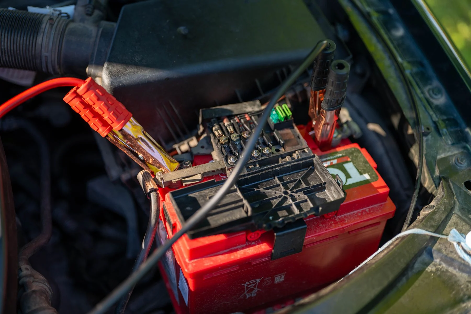 Illustrative stock photograph of automotive battery terminals and electrical connections in an engine bay outdoors