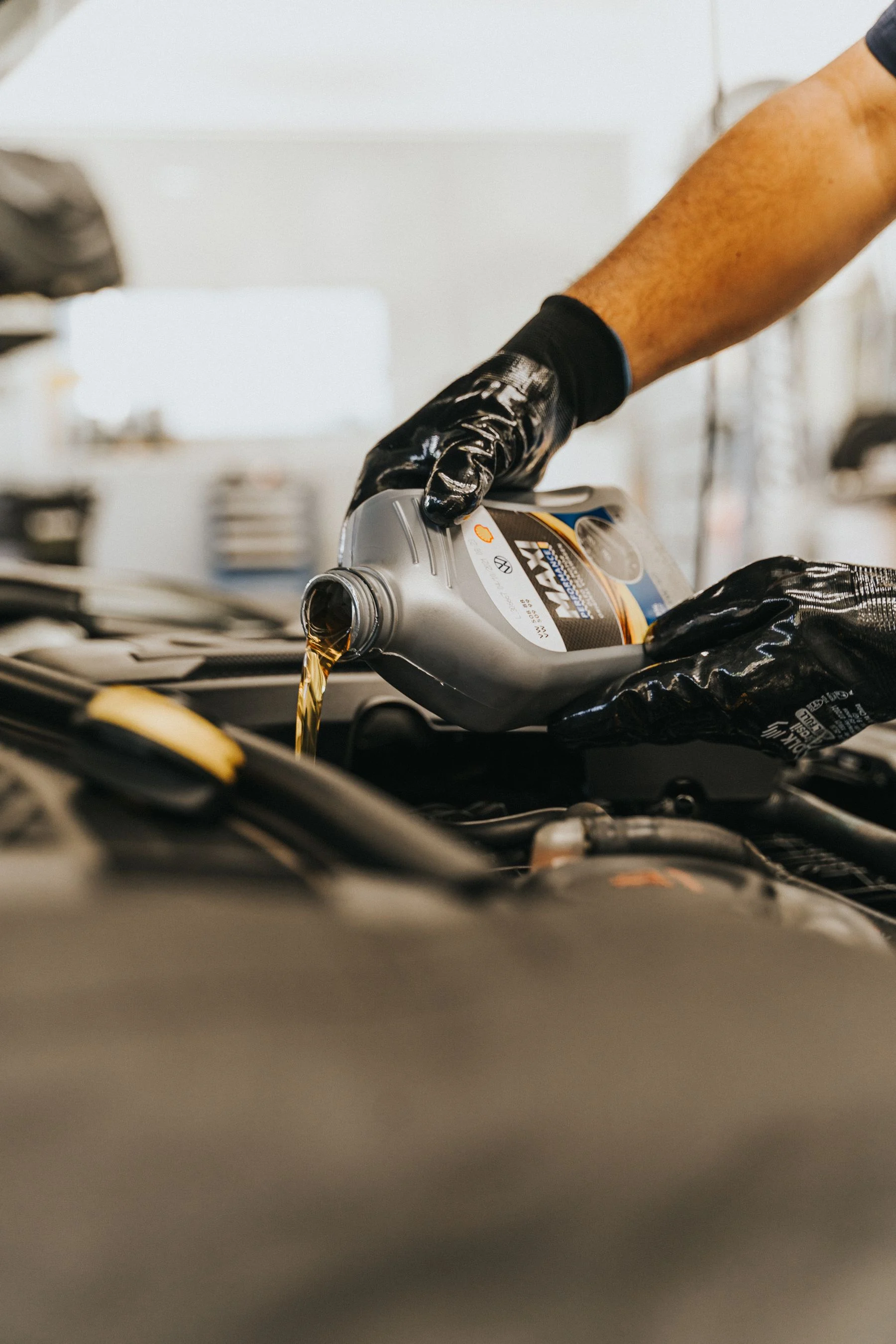 Stock photograph of gloved hands pouring fresh motor oil into a vehicle engine