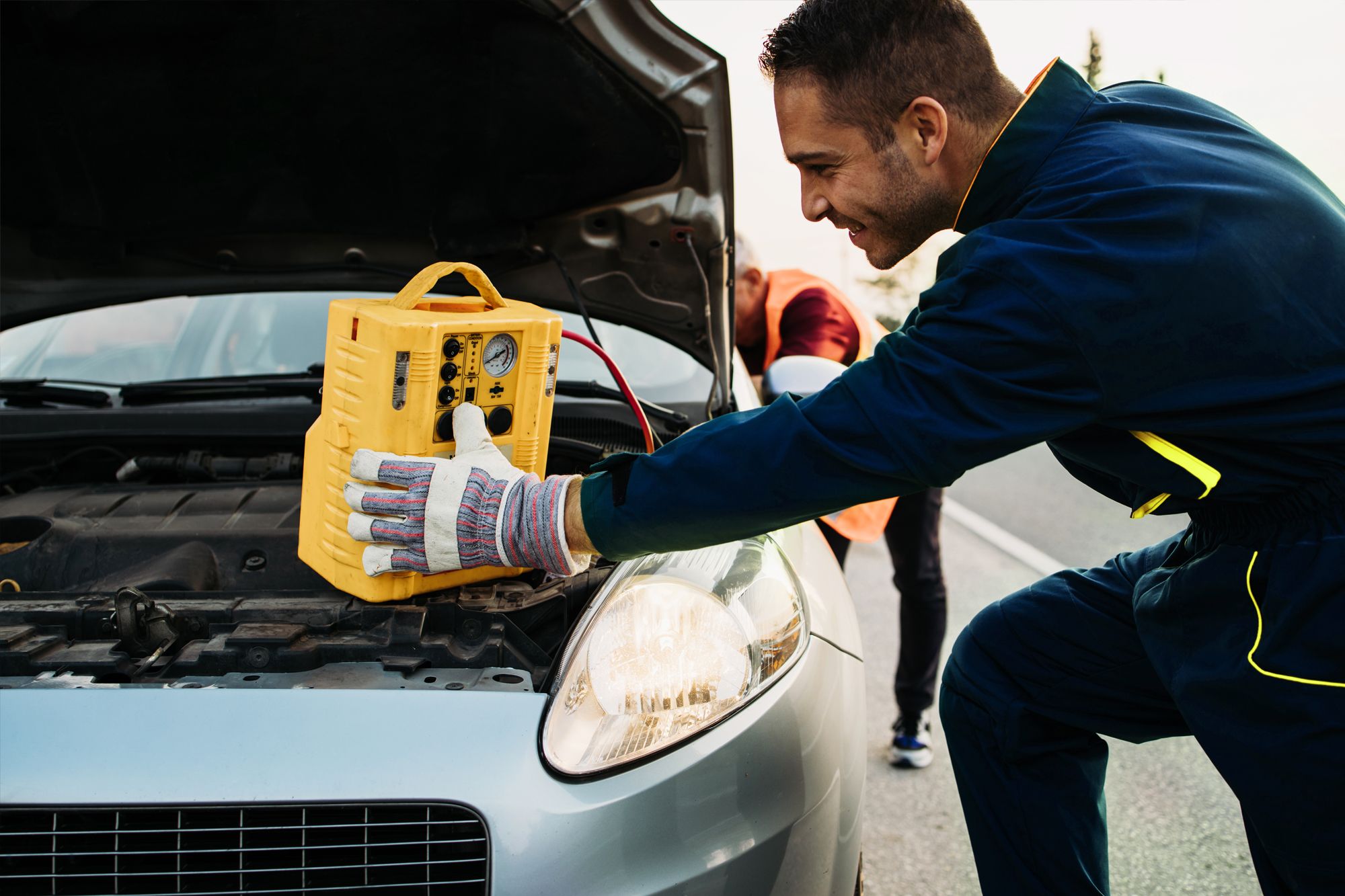 Illustrative photograph of roadside charging assistance at a passenger vehicle engine bay