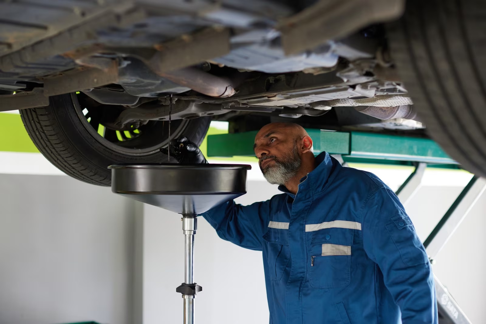 Illustrative photograph of a mechanic draining engine oil from underneath a passenger vehicle