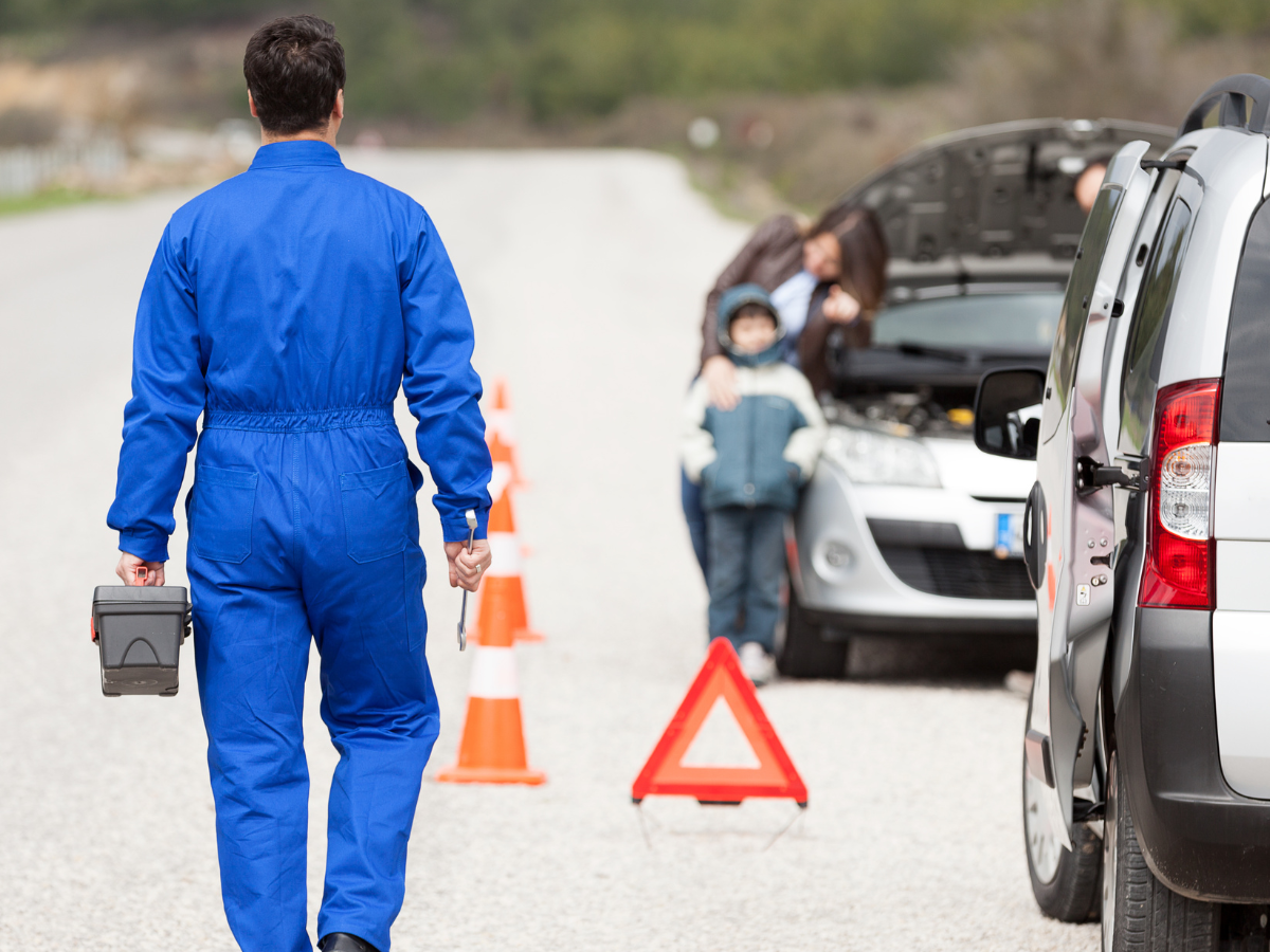 Illustrative photograph of a mobile mechanic carrying tools toward a roadside passenger vehicle with its hood open